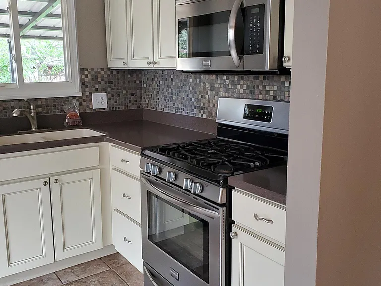 View of kitchen showing custom cabinets, gas range and microwave. Kitchen no longer has ceramic tile flooring - it now has new luxury vinyl flooring.