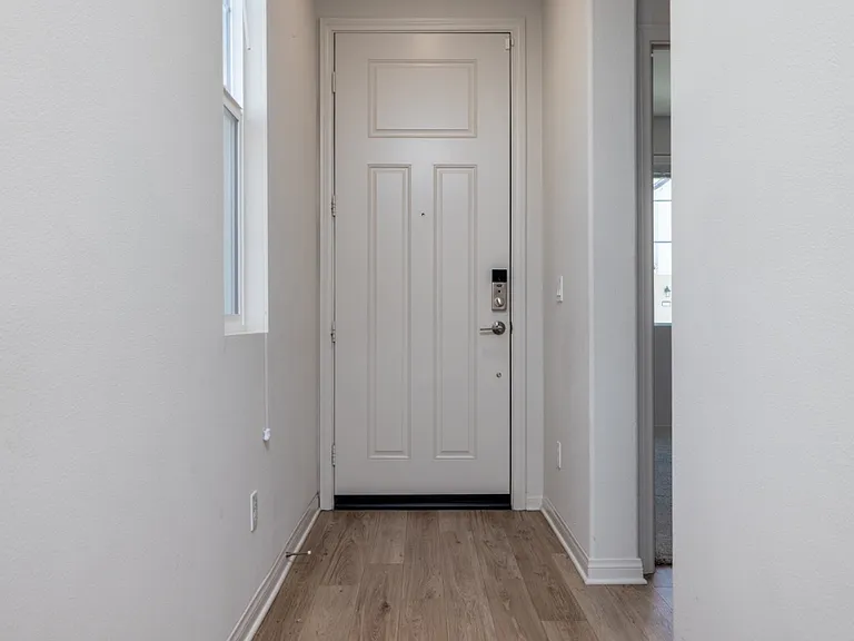 Bright and welcoming entryway with laminate flooring and modern white door, creating a clean and inviting first impression that leads seamlessly into the home's open layout.