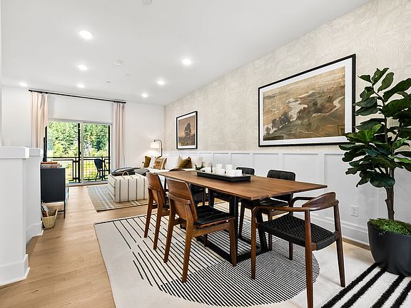 A modern and minimalist dining room with a wooden table, chairs, and a large framed artwork on the w