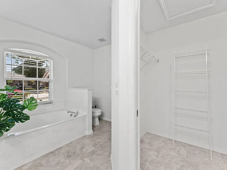 Spacious bath features a soaking tub with large window and an adjacent walk-in storage closet with built-in shelving.