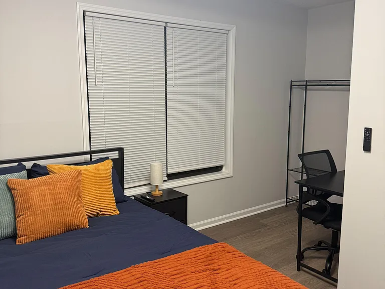 Private bedroom with a comfortable bed, large window with blinds, and a dedicated desk area for work or study.