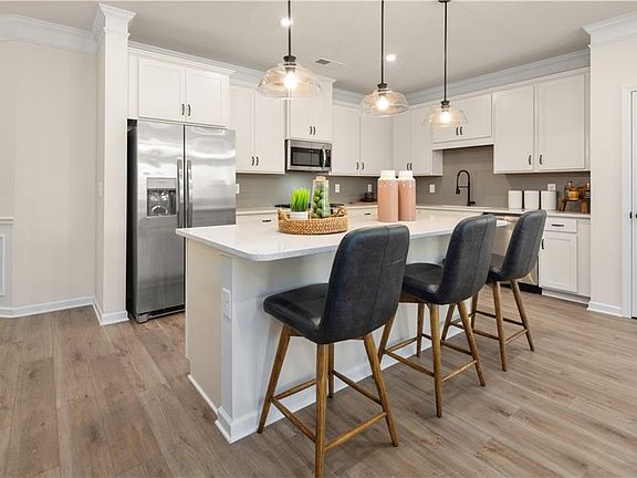 Kitchen featuring white cabinetry, light countertops, ornamental molding, a center island, and appl