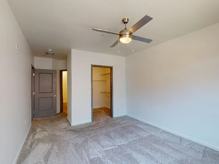 Spacious apartment bedroom with large closet, attached bathroom and plush carpet flooring.