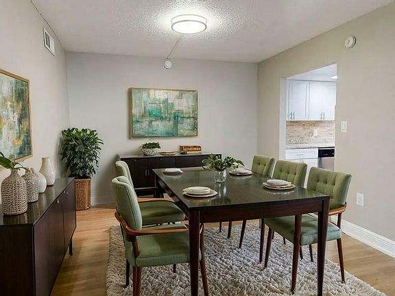 Elegant dining room with modern decor and a plush rug, featuring a stylish wooden table with vibrant green upholstered chairs and contemporary artwork.