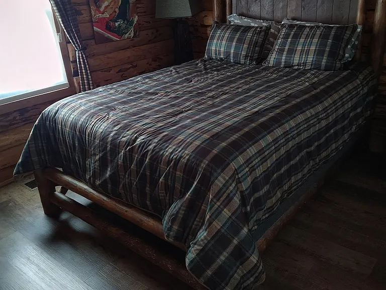 Bedroom with rustic wood plank walls, a sturdy bed frame, and a window with curtains for natural light and privacy.