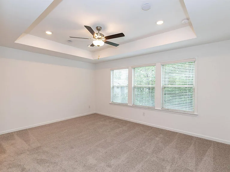 Spacious bedroom with plush carpet, large windows, and a ceiling fan
