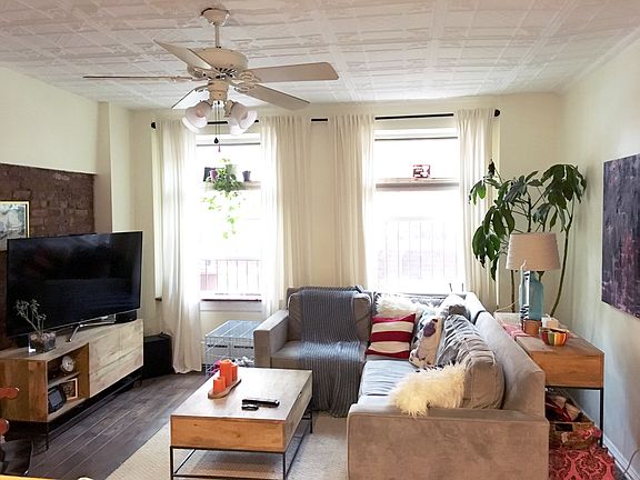 Living room has hardwood flooring, tin ceiling, fan, exposed