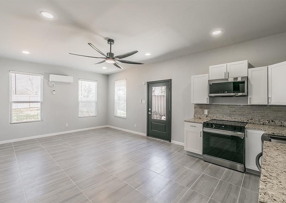 Kitchen with a wall mounted AC, stainless steel microwave, decorative backsplash, electric range, and a ceiling fan