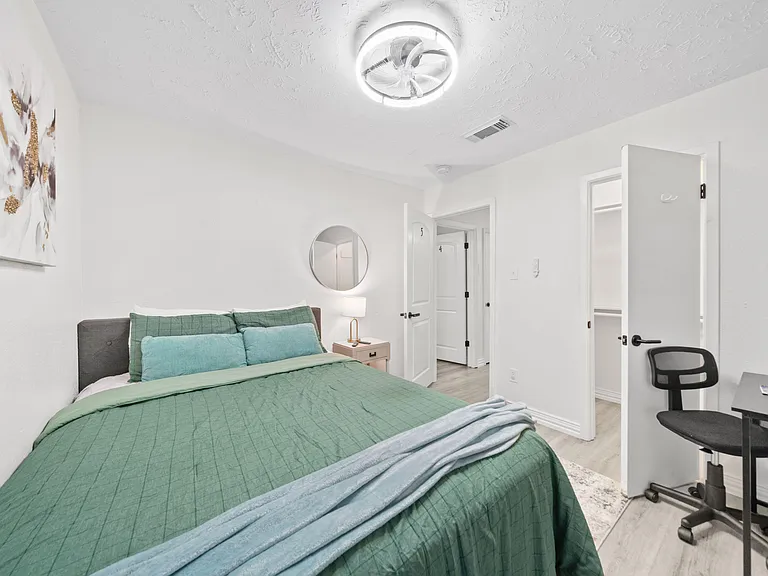 Well-appointed bedroom featuring a full bed, nightstand lighting, dedicated desk area, and an open closet for easy storage.