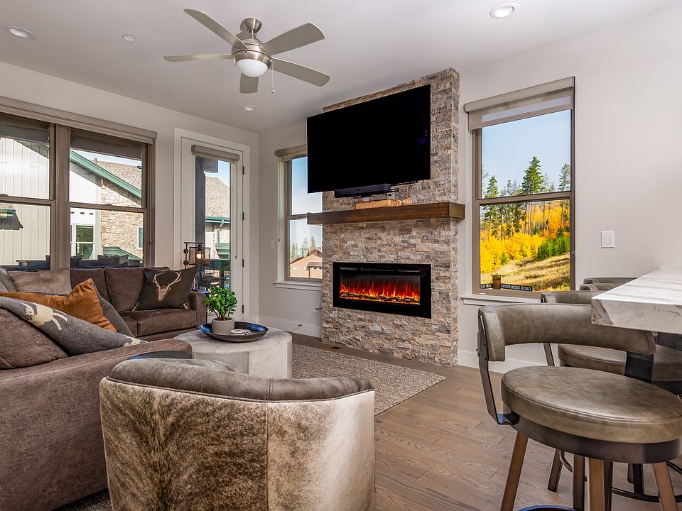 Beautifully furnished living room featuring a stone fireplace, large windows, and sweeping mountain views for the perfect cozy retreat!