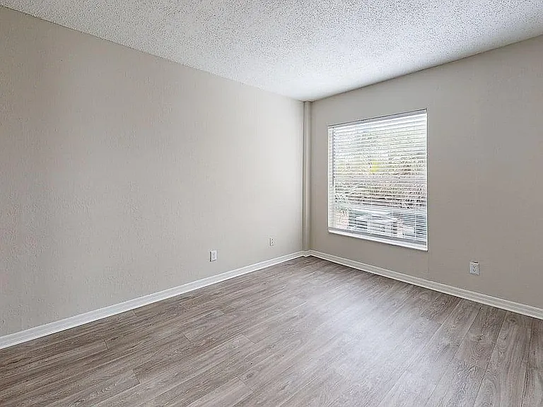 Bright and spacious empty room with large window and sleek hardwood floors, ready for customization in a modern home.