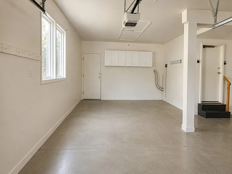 View of large area for workbench at back of garage as well as drop down stairs for access to lighted storage area above garage.