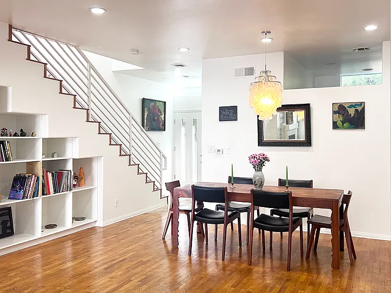 Bright open-concept living and dining space featuring real wood floors, accented by high ceilings with curated recessed lighting, artistic designer furniture, and chandelier.