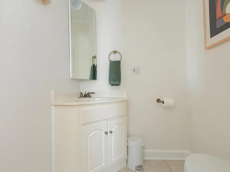 Small half bath with toilet on the right, corner sink with storage underneath, and a corner mirror / medicine cabinet with good storage. Overhead is a pendant light not pictured.