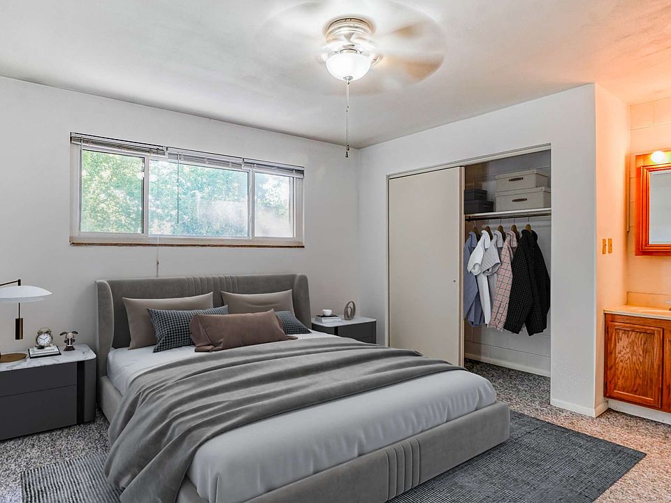 A light room with a ceiling fan, window, air conditioner, and grey carpet, featuring a closet and plain walls.