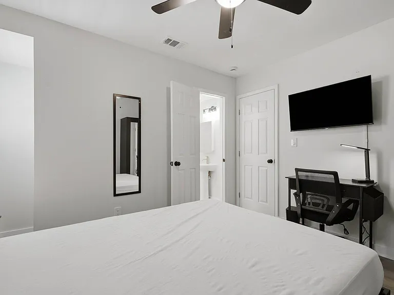 Well-appointed bedroom with ceiling fan, wall-mounted TV, dedicated desk area, and nearby bath access for convenience.