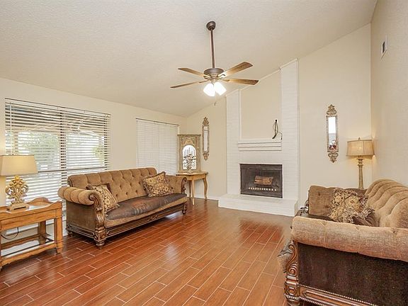 Large living room with durable wood-look tile flooring and high ceiling. Windows overlook the covered patio