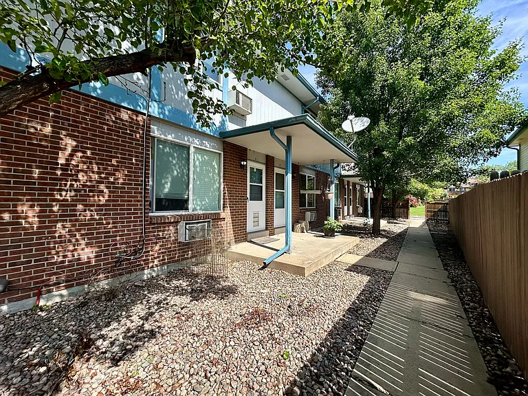 Charming brick apartment exterior with lush greenery and a cozy concrete patio.