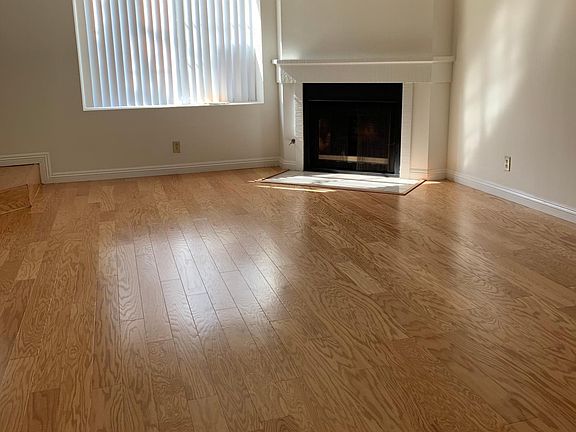 Living room with corner fireplace as main feature, as well as a large window which has a wide sill, perfect for house plants