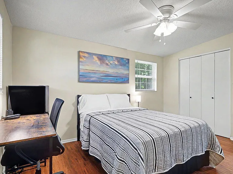 The bedroom includes a full bed, work desk w/lamp, TV, ceiling fan, and a roomy closet, and 2 windows offering natural light.