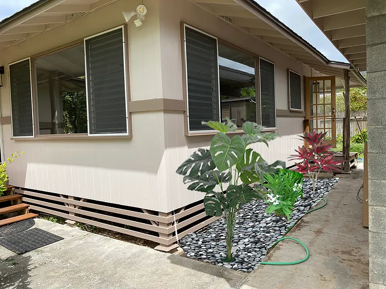 Charming beach house exterior with fresh landscaping, tropical accents, and covered walkways. Large windows fill the home with natural light while creating a bright, airy indoor-outdoor island living experience. _____