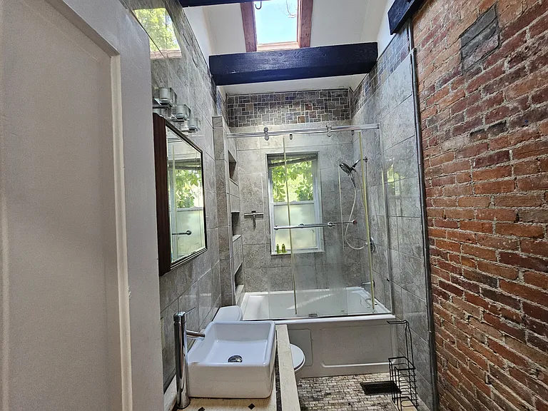 Exposed brick and very fancy tile all throughout the bathroom. Modern sink light fixtures and large exposed rustic wooden beams.