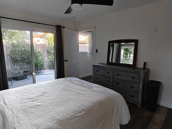 Bedroom with ceiling fan, dresser and mirror, plus sliding glass door and window with views to a private patio.