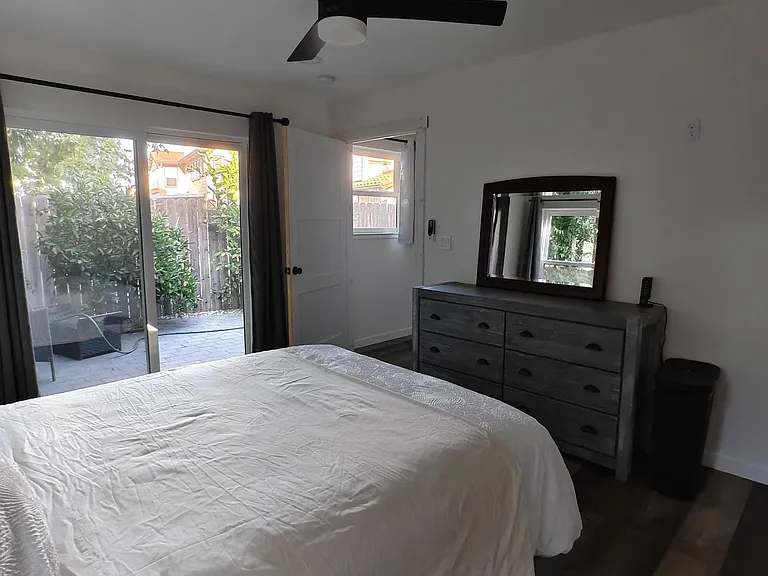Bedroom with ceiling fan, dresser and mirror, plus sliding glass door and window with views to a private patio.