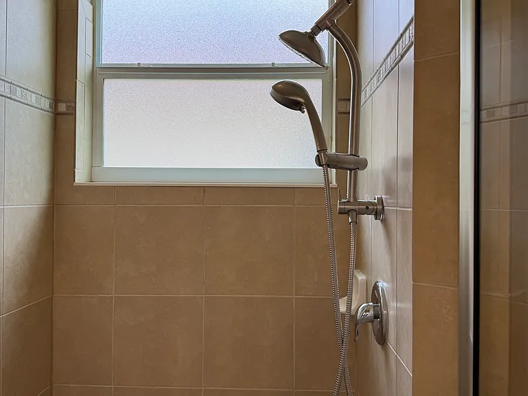 Large tiled shower with new shower heads and grab bars