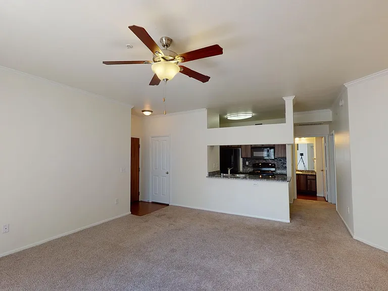 Apartment kitchen, dining room, and living room with plush carpet flooring.
