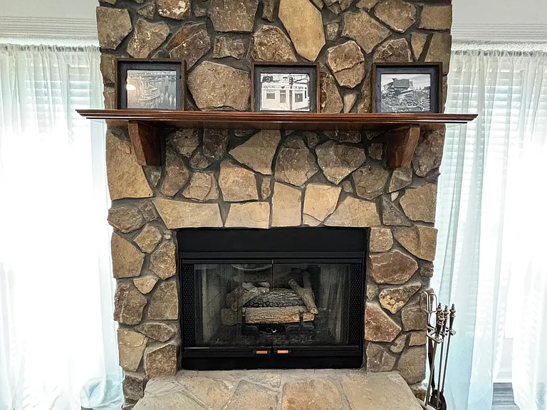 Living area focal point featuring a stone fireplace with raised hearth and mantel, flanked by large windows.