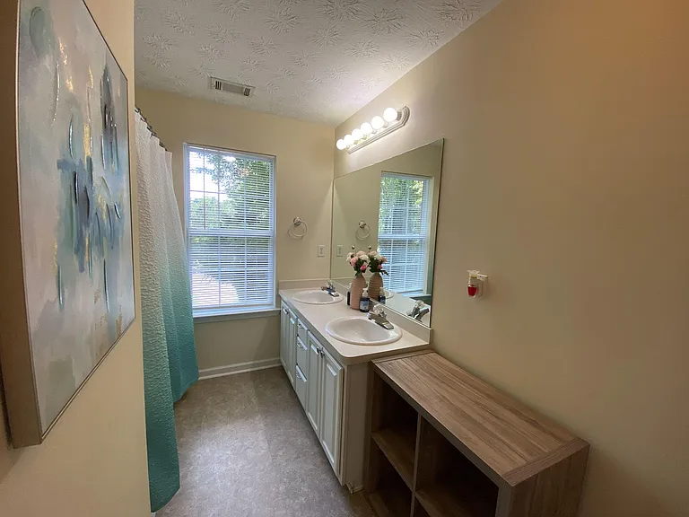 Full bathroom with double-sink vanity, large mirror, and a window for natural light plus ample under-sink storage.
