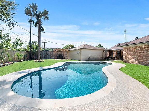 View of AWESOME Backyard. Enjoy a tropical vacation at home! Palm trees and pretty blooming landscaping. Wood privacy fence. Wonderful pergola behind garage with cement pad is perfect spot for grilling.