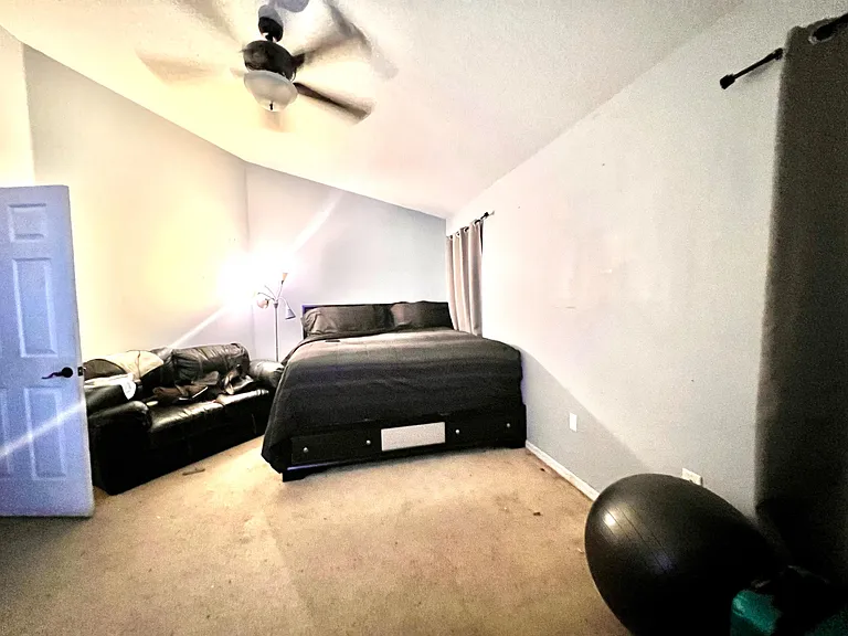 Spacious bedroom with a ceiling fan, large bed area, and room for seatingideal for relaxing and studying.