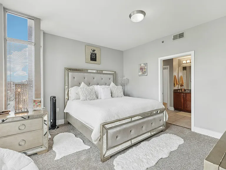 Primary bedroom with large windows, plush carpeting, and mirrored furniture.