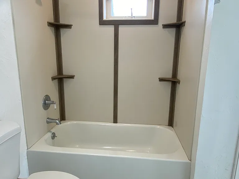 A functional bathtub/shower unit enhanced by corner storage shelves and a high, operable window that provides natural light and ventilation with excellent privacy.