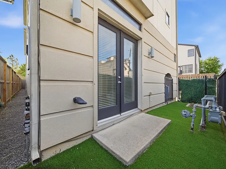 Narrow, low-maintenance side yard featuring artificial turf and a clean, modern design. Framed by a privacy fence and a sleek exterior with double glass doors, the space offers a functional outdoor area with easy upkeep.