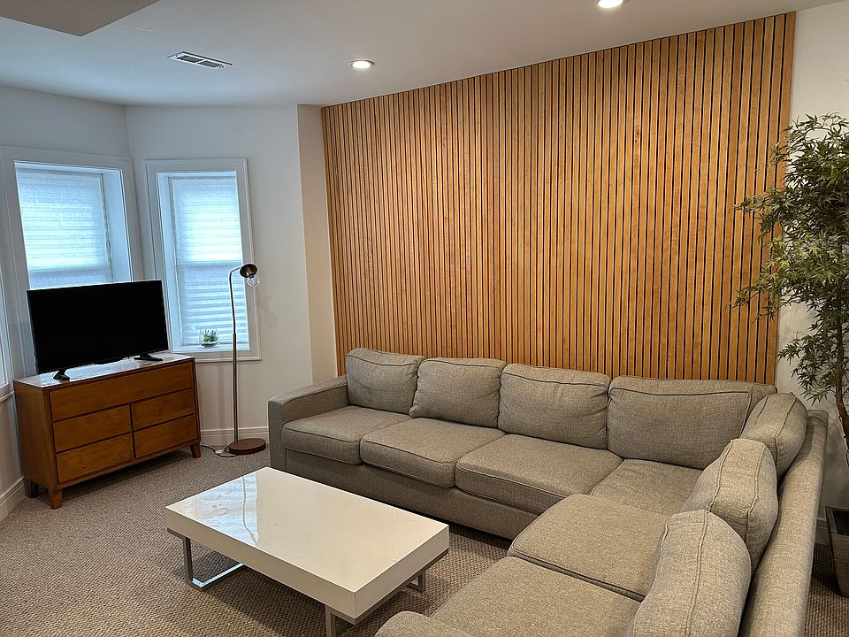 Living room with oversized L shaped couch, custom mid-century paneled wall, and smart TV