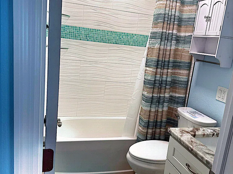 Updated full bath with tiled tub/shower, storage cabinet, and a vanity with stone-look countertop for daily convenience.