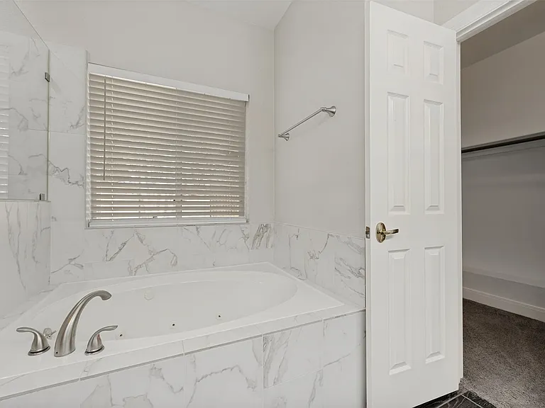 Corner soaking tub encased in white marble-finish tile, featuring brushed nickel fixtures