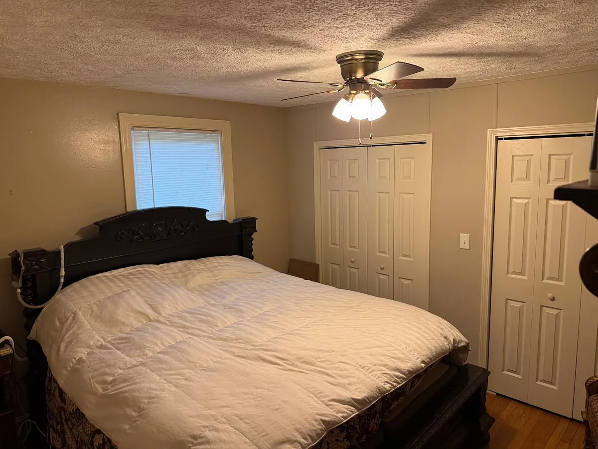 Photo 1 of 6 - Castle Heights Ave - Lebanon, TN Bedroom with a queen bed, ceiling fan light, window with blinds, and double-door closets for storage. - Castle Heights Ave