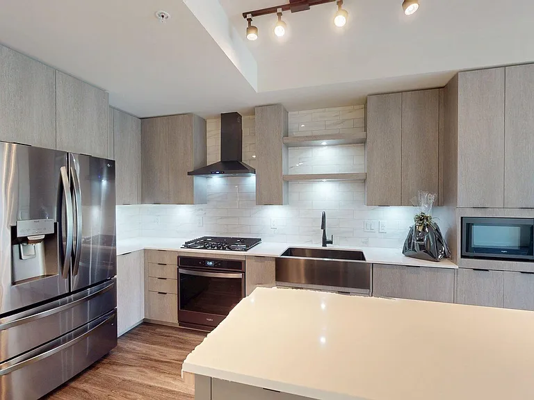 Apartment kitchen with black stainless steel appliances, quartz countertops, wood-style flooring, and custom Italian cabinetry.