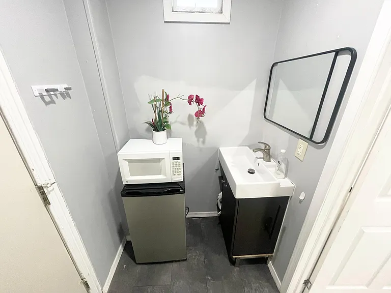 Compact wash area with pedestal sink, wall mirror, and space for small appliances for added convenience.
