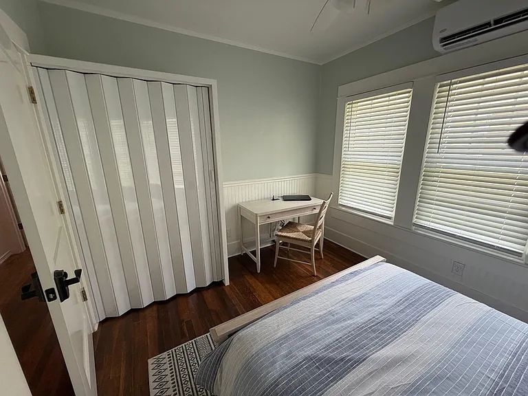 Bedroom with hardwood floors, wide windows with blinds, and a dedicated desk area plus closet storage for easy living.