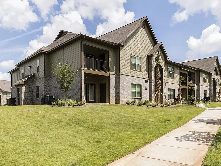 Charming modern apartment community with lush green lawns and picturesque palm trees under a bright blue sky.