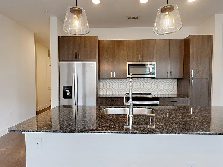 Apartment kitchen with stainless steel appliances, granite countertops, and wood-style flooring.