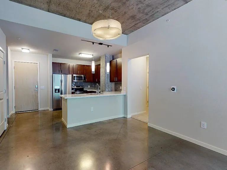 Apartment kitchen with stainless steel appliances, dining and living room with polished concrete flooring.