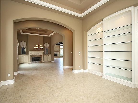 Just to the right of the entry is the formal den. Custom glass shelves with light is the perfect display space for collector items or special family memorabilia. Trey ceilings and archways create an open concept floor plan with views into the formal 
