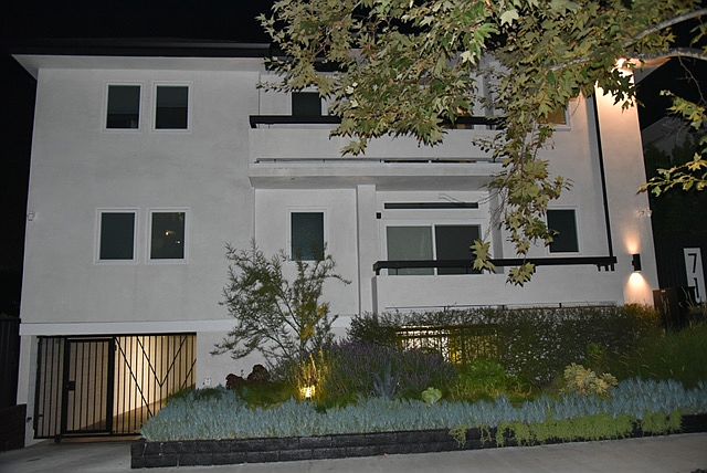 Nicely lit front exterior of the building at night on a tree lined street with mostly expensive single family homes.