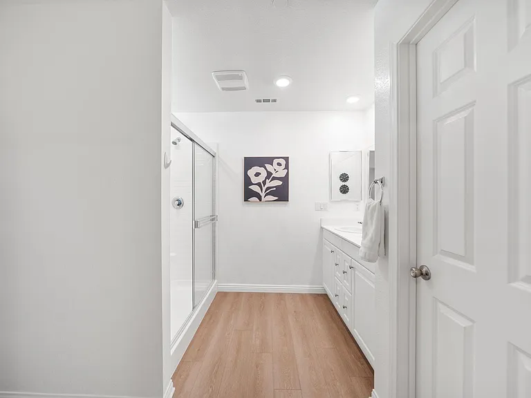 Full bathroom with glass-enclosed tub/shower, long vanity with ample storage, and recessed lighting.